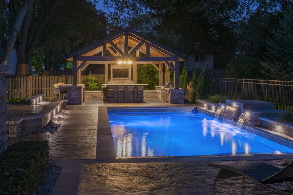 Night time view of inground pool with large outdoor cabana